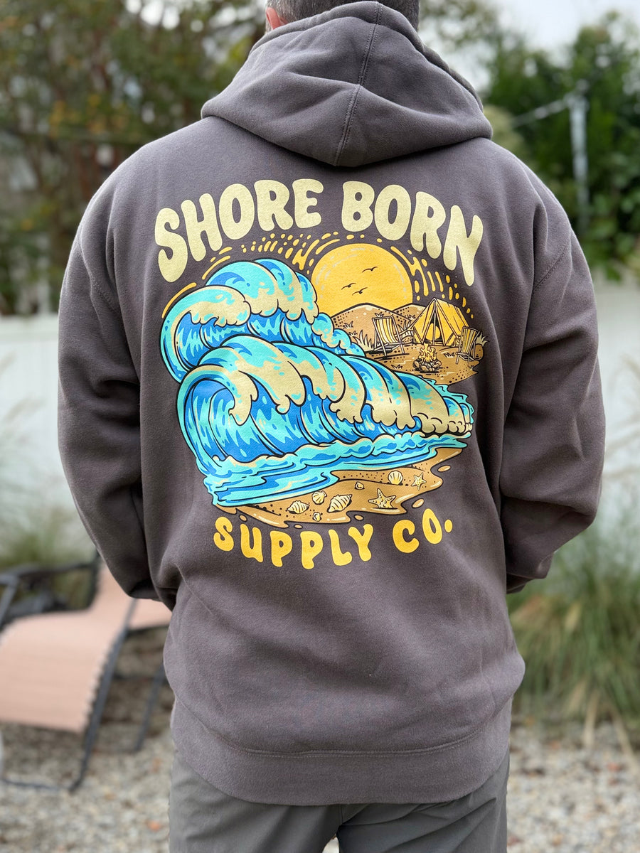 Person wearing a hoodie with 'Shore Born Supply Co.' design on the back outdoors.